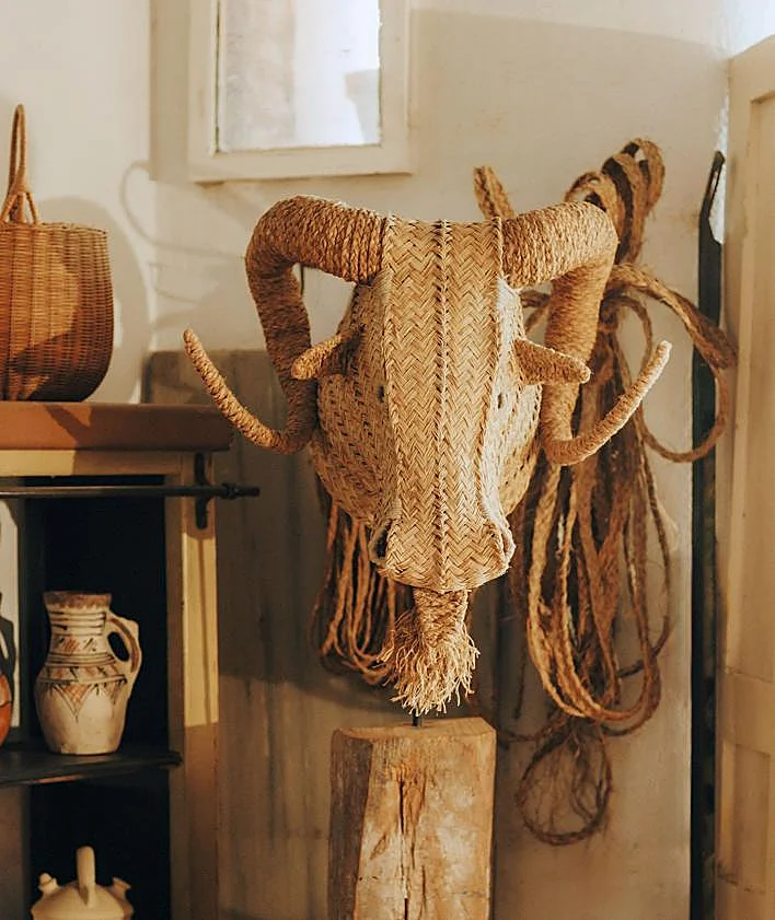 Imagen secundaria 2 - Interior del taller decorado con lámparas industriales. Encima, estantería antigua con cestos y bases de cabezas; y, a la derecha, jarrones de barro, y en la pared, cartel de una antigua taberna con más cabezas de animales, botijos y cestas. 
