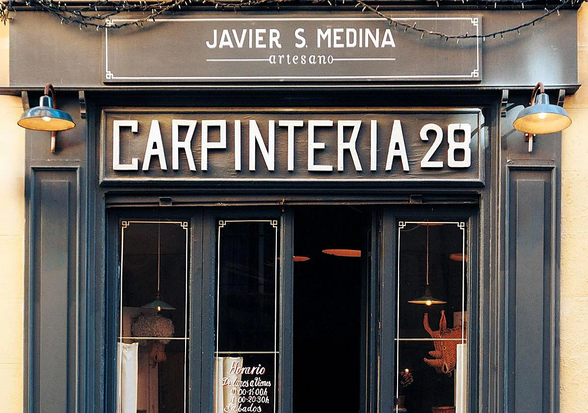Imagen principal - Sobre estas líneas, la fachada del taller, enclavado en el barrio de Malasaña, en Madrid, que conserva el cartel de una carpintería que albergó en tiempos este local. Las vitrinas las recuperó Javier de una antigua tienda.